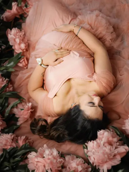 A dreamy overhead shot of a mother-to-be lying in a bed of pink flowers and soft tulle.