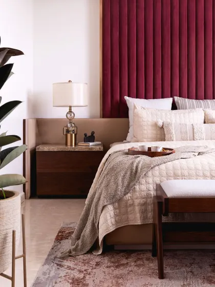 The deep red headboard contrasts beautifully with the neutral walls and soft, cream-colored bedding. A large plant adds a touch of nature and freshness to the room.