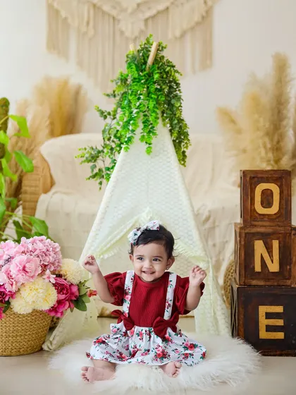 A one-year-old girl celebrates her birthday in a boho-themed studio setup, complete with a teepee and "ONE" blocks. Her excited expression perfectly captures the milestone.