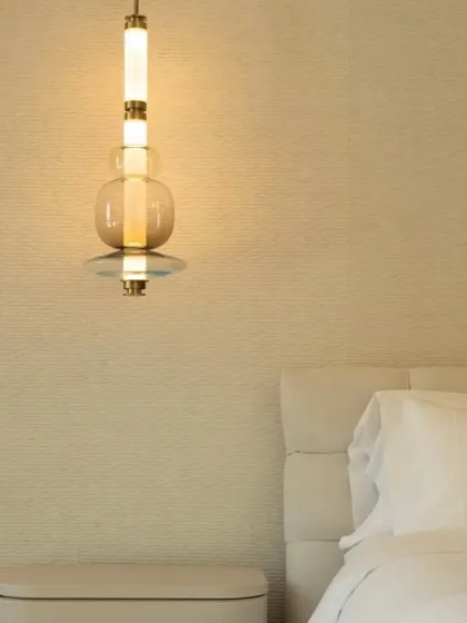 A detailed view of a single Luna Kaleido pendant next to a bed, highlighting the quality of the hand-blown glass and the warm, ambient light it produces.
