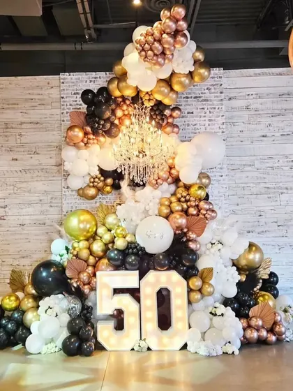 A grand and glamorous 50th birthday setup. This stunning display features a massive organic balloon arrangement in black, white, and metallics, a crystal chandelier, and a large light-up '50'.