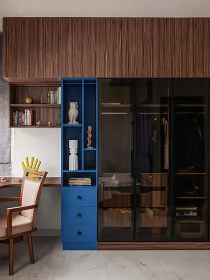 The son's bedroom in 'Project Varnika' is a mature yet youthful space, combining bold navy blue with warm wood tones. The layout is designed to maximize the view of the lush greenery outside.