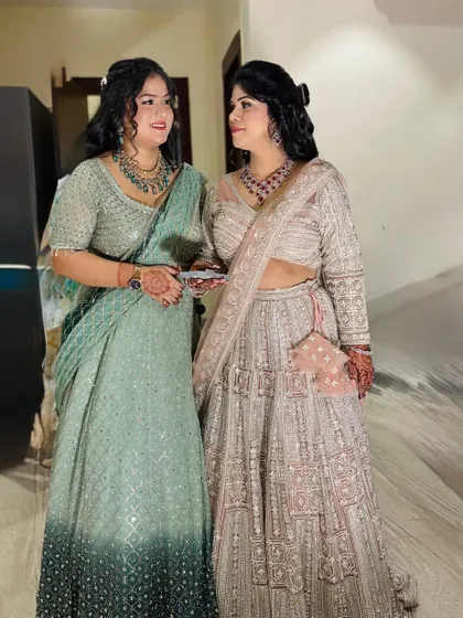 A full-length shot of two sisters, one in a lehenga and one in a saree, both with beautiful party makeup.