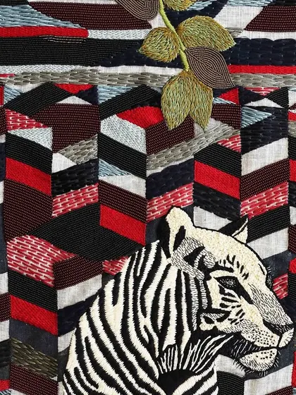 A detailed shot of the "Tiger in his Red Forest" tapestry. The bold red and black geometric background creates a powerful contrast with the calm demeanor of the tiger, highlighting him as the protagonist of his world.