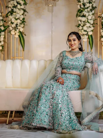 Supriya relaxing on a couch, the full flare and sparkle of her reception lehenga on display.