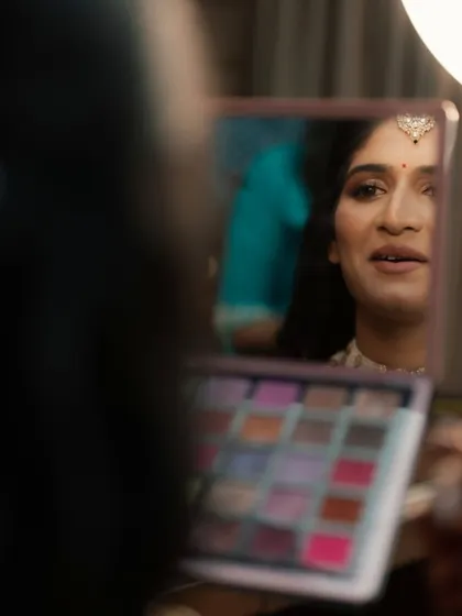 A creative shot showing the bride's reflection as she looks at the eyeshadow palette, capturing the artistry of the process.