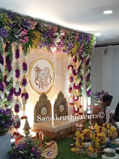 A wider view of the cow-themed setup during a pooja. The lush floral arch and side arrangements create a complete and immersive sacred space for the ceremony.