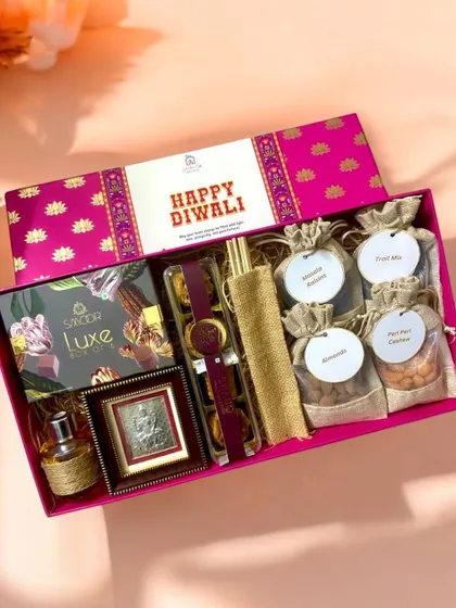 A closer look at the premium Diwali hamper, showcasing the rich textures and vibrant colors. It includes Smoor luxe chocolates, a silver Lakshmi ji frame, a lavender reed diffuser, and small jute potlis filled with assorted dry fruits.