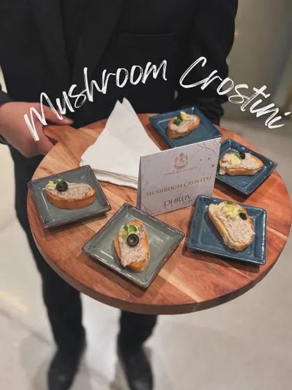 My Mushroom Crostini, served on a wooden platter by a member of my professional staff. Toasted bread is topped with a creamy, savory mushroom spread and a black olive garnish.