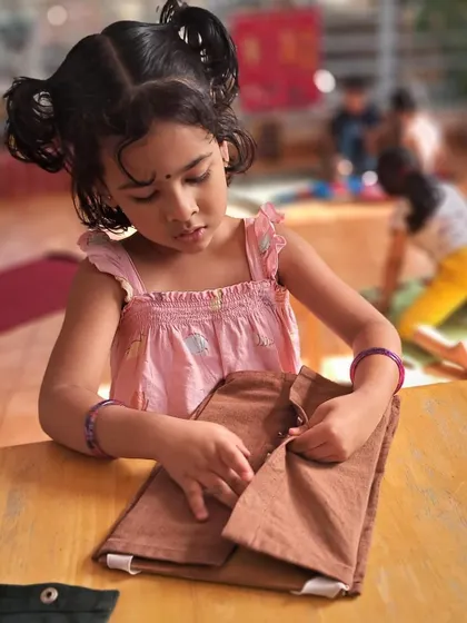 A girl practices buttoning on a dressing frame. Mastering this skill gives her the confidence and ability to dress herself, a significant step towards independence.