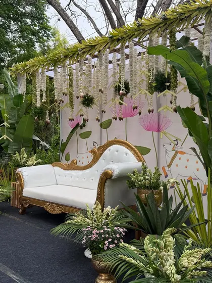 A close-up of the Pichwai-themed baby shower decor, featuring a classic white chaise lounge set against a backdrop of lotus flowers and cows.