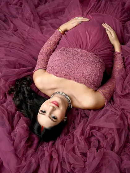 An artistic overhead shot. The mom-to-be lies on a sea of mauve fabric, creating a beautiful composition that highlights her serene expression and the rich color of the gown.