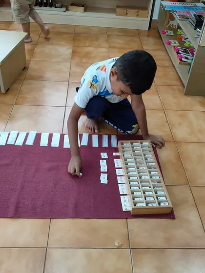 A child works with a large set of number tiles on a work mat. This quiet, focused activity is an example of how children can engage in complex mathematical work when they are interested and the materials are presented clearly.