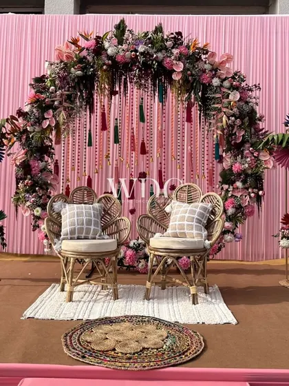 The couple's seating for the Mehendi, featuring two beautiful peacock chairs set against a circular floral arch with hanging tassels. The setup is both bohemian and romantic.