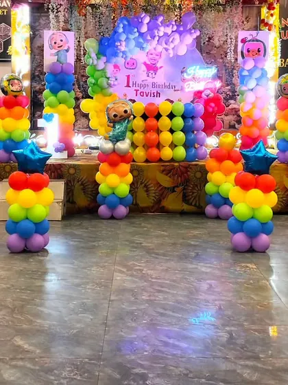 The complete Cocomelon themed stage setup with rainbow balloon pillars topped with star-shaped foil balloons. This bright and cheerful decoration is perfect for a first birthday celebration.