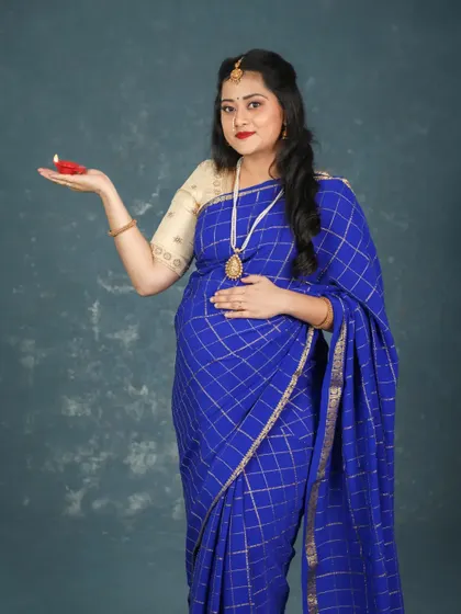 A festive and hopeful portrait of a mom-to-be in a blue saree, holding a small lit diya. This image beautifully combines traditional elements with the celebration of new life.