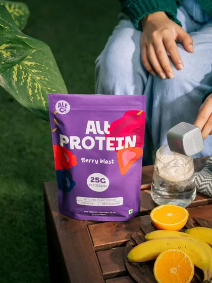 A lifestyle scene of Alt Co.'s Berry Blast protein being prepared for a post-workout drink. The fresh fruits and outdoor table setting suggest a healthy and enjoyable routine.