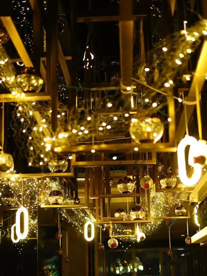 The ceiling of a venue transformed for a 40th birthday party. The industrial-style ceiling is decorated with a web of fairy lights and hanging glass baubles, creating a stunning and magical effect.