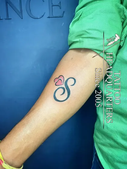 A simple yet elegant initial "S" tattoo with two small hearts, perfect for a minimalist and personal statement.