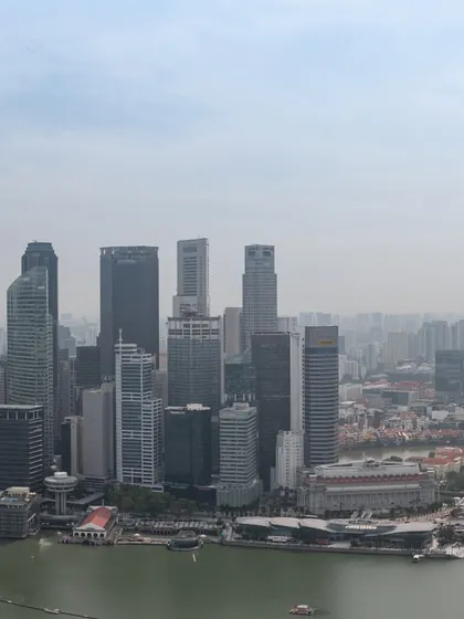 A daytime photograph of the Singapore skyline, showing the dense cluster of skyscrapers in the central business district.