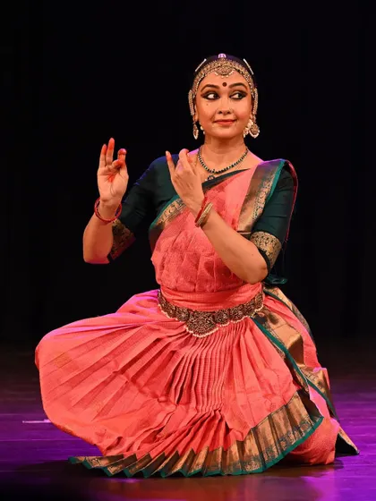 A seated pose from a Bharatanatyam performance, demonstrating the flexibility and control required. The dancer's expression is one of serene confidence.