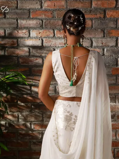 The back of this white lehenga blouse features a deep V-cut with delicate tassels, adding a touch of modern allure to a timelessly elegant ensemble.