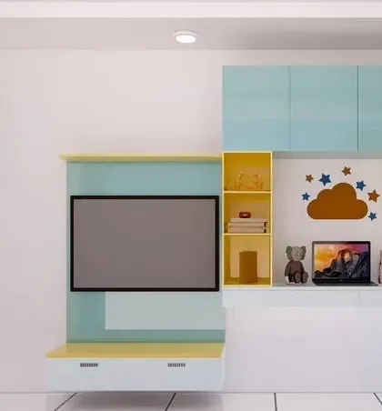 The entertainment and study zone in the kids' room. The TV unit is designed with playful colors and includes open shelves for books and toys, along with a dedicated laptop space.