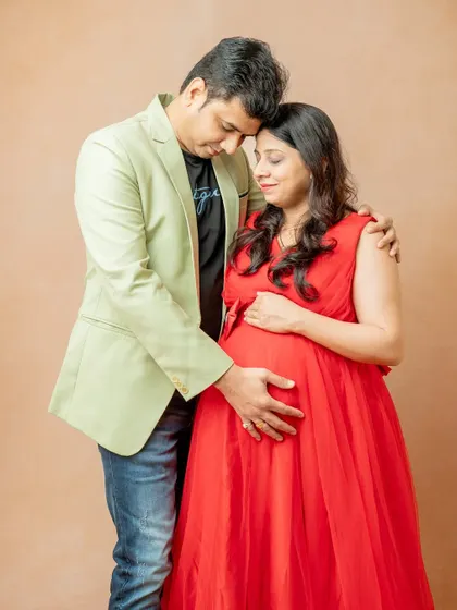 An intimate moment between the couple. The partner rests his forehead against hers, both gently holding the baby bump, creating a feeling of unity and shared love.