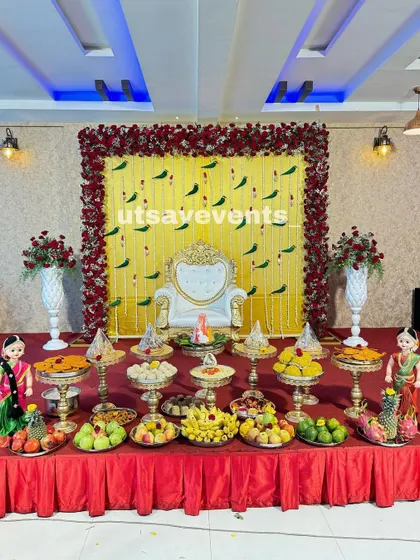 Here is a vibrant and classic baby shower decoration. The stage is set with a bright yellow backdrop adorned with hanging parrot motifs and framed by a rich border of red roses, creating a festive and traditional South Indian look.