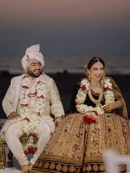 The couple shares a laugh while seated at the mandap, a candid moment of joy amidst the formal rituals.