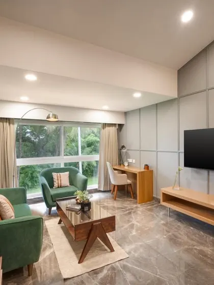 This suite's living area combines comfort and style with plush green sofas, elegant grey wall paneling, and marble-finish flooring. The layout includes a dedicated work desk, making the space versatile for both relaxation and productivity.