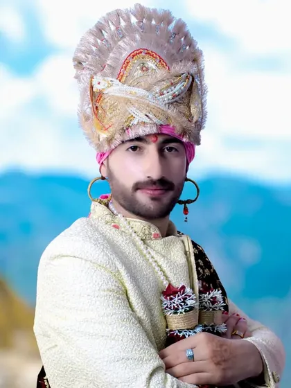 A confident portrait of the groom with his arms crossed, highlighting the beautiful details of his traditional headwear.