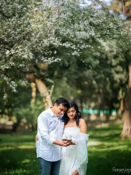 A couple sharing a sweet moment under a canopy of white blossoms. This image captures the romance and tenderness of awaiting a new life together.
