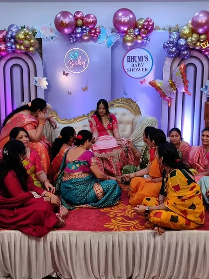 The ladies gather on stage to perform a traditional 'godh bharai' ritual, showering the mom-to-be with blessings and gifts.