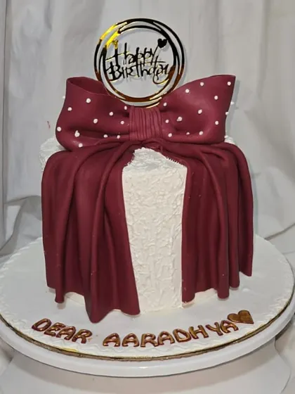 A cute cake for a sweet celebration. This design features a rich maroon fondant bow over a textured buttercream base, personalized for Aaradhya's birthday.