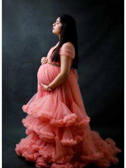 A side profile portrait in a pink ruffled gown against a dark backdrop. This pose is perfect for emphasizing the beautiful silhouette of pregnancy.