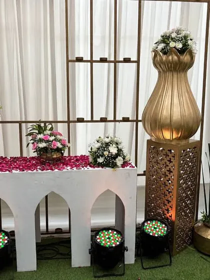 A traditional decor setup on a white arched table, featuring golden vases, flower petals, and intricate pedestals, creating an elegant and sacred corner.