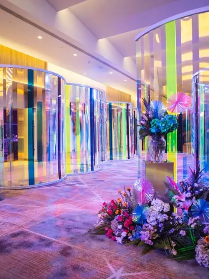 The full view of the iridescent tunnel entrance, lined with stunning, colorful floral arrangements. The design guides guests through a journey of color and light before they even reach the main event space.