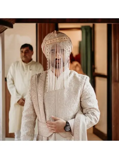 The groom, with his face partially covered by the sehra, makes his way to the ceremony. This shot captures the traditional and suspenseful moments before he sees his bride.