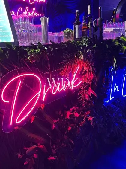 A bar that sets the mood. We used lush greenery and fun neon signs like 'Drunk In Love' to create a lively and photogenic beverage station.