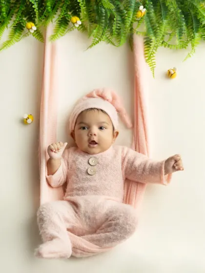 This little one is wide awake and curious in a pink swing setup, surrounded by greenery and cute bumblebee props.