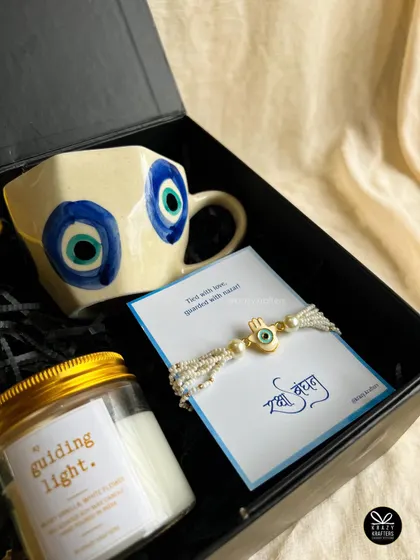 A close-up of the 'Jigar Ka Tukda' evil eye themed hamper, showing the hand-painted mug and matching rakhi.