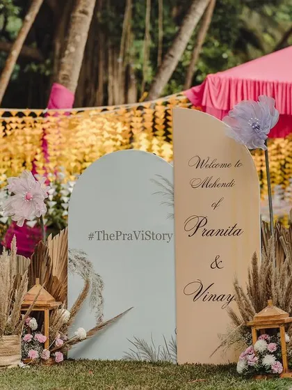 A personalized welcome sign for a Mehendi, set against a backdrop of colorful drapes and pampas grass, perfectly capturing the boho-chic vibe of the event.