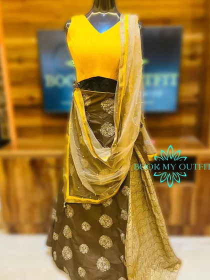 A unique lehenga combining a simple yellow blouse with a brown skirt featuring silver floral patterns. The sheer dupatta adds a touch of grace to this party wear outfit.