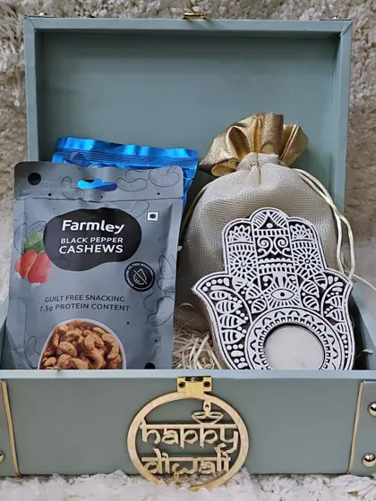 An open view of the healthy gifting trunk. It's curated with Farmley black pepper cashews, a potli of mixed nuts, and a serene Hamsa-hand tealight holder.