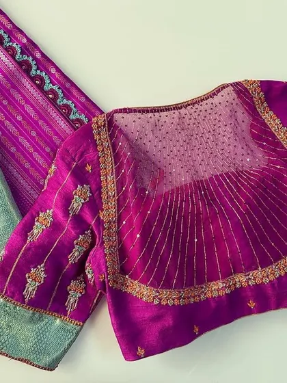 The back of the magenta blouse features a sheer panel with a sunburst pleat design, adding a unique and modern detail.