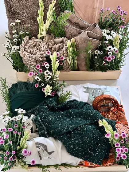 A pair of trousseau trays featuring dark green and brown outfits, both lavishly decorated with fresh flowers for a luxurious and organic feel.