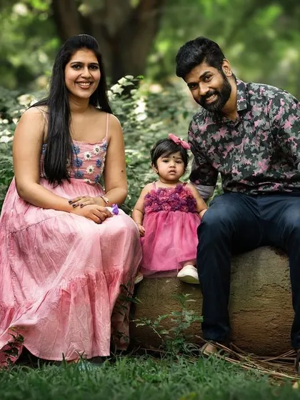 A family portrait set against the lush greenery of a park. Posing on a log, this family of three shares a relaxed and happy moment together.
