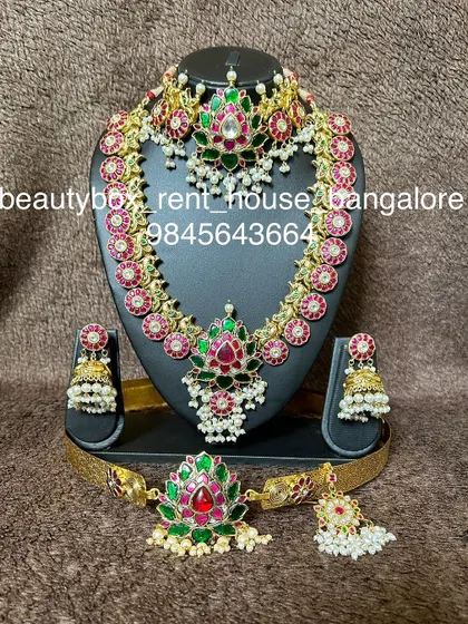 This kemp stone set features a beautiful combination of red and green stones with pearl drops. The rental includes a choker, haaram, and matching accessories.