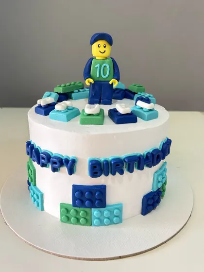 A fun Lego-themed cake with a custom fondant minifigure and colorful edible blocks surrounding the cake.